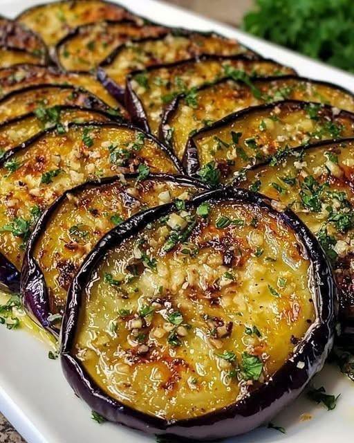 A close-up shot of golden-brown Lemon Garlic Roasted Eggplant cubes garnished with fresh parsley and lemon slices.