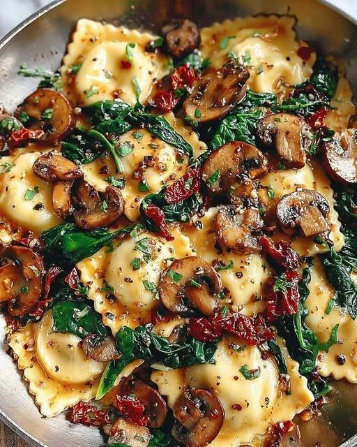 A top-down view of a skillet filled with easy cheesy ravioli tossed with sautéed mushrooms, fresh baby spinach, and sun-dried tomatoes.