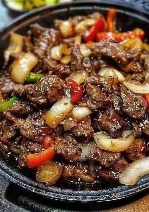 A sizzling hot cast iron platter loaded with Sizzling Chinese Pepper Steak, crisp bell peppers, and sliced onions in a dark savory sauce