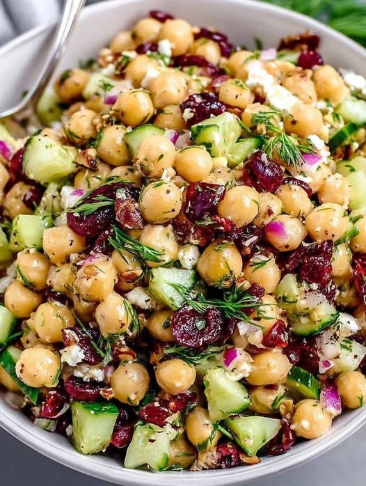 A colorful bowl of Mediterranean bean salad featuring chickpeas, black-eyed peas, diced cucumbers, and feta cheese.